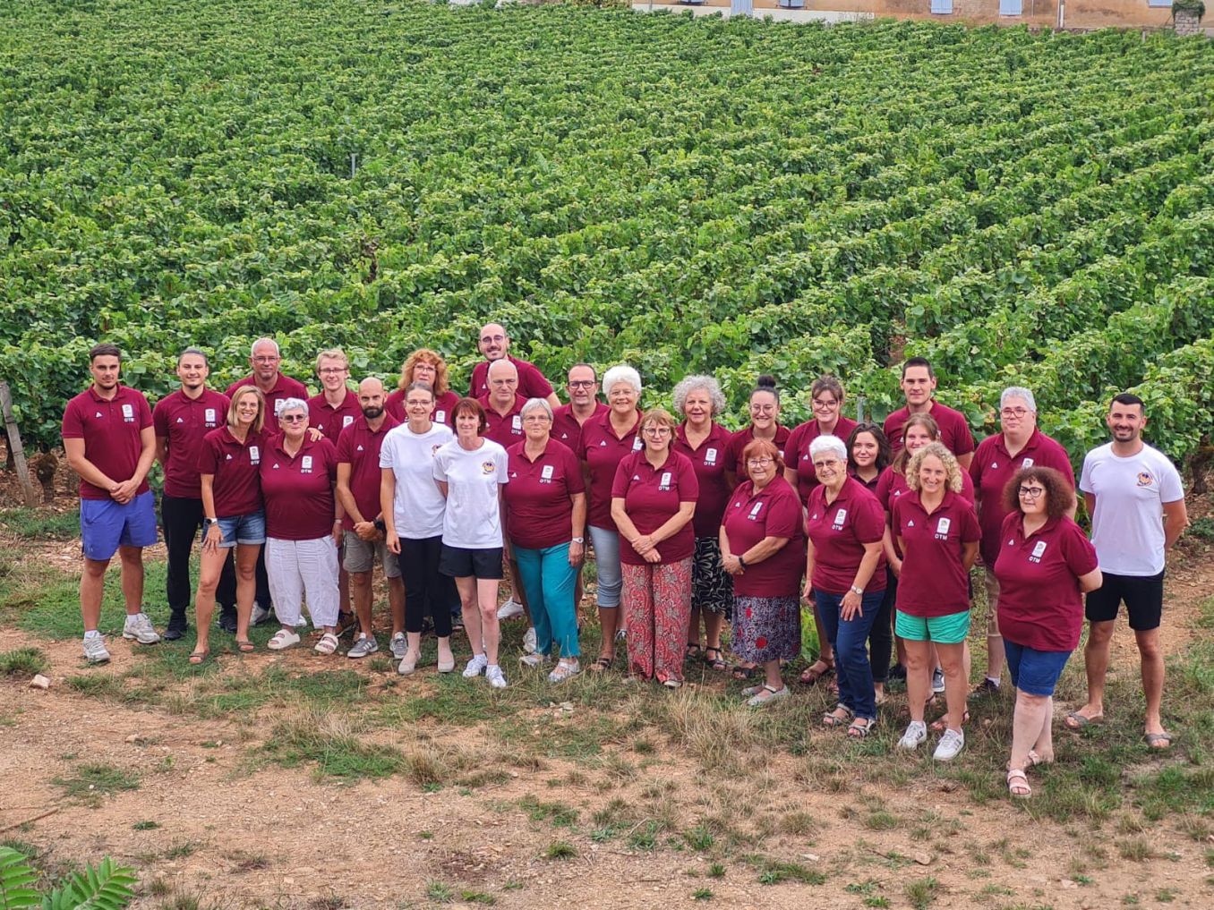 Photo de groupe des officiels de table de marque, en polo bordeaux « OTM », devant des vignes.